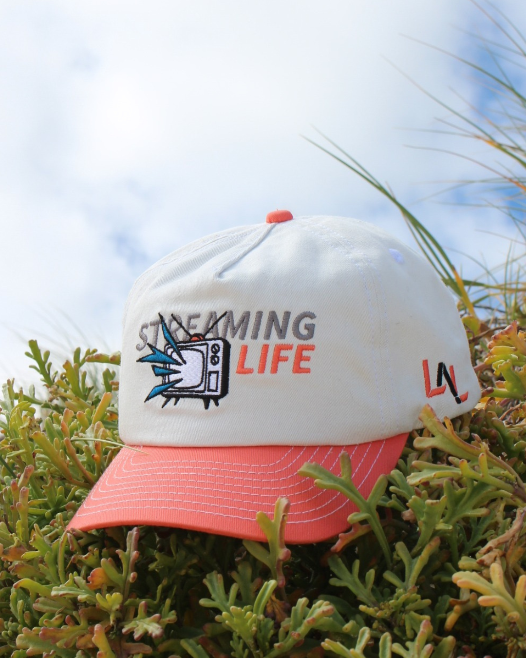 Streaming Life Cap embroidered logo detail on coral and white cap outdoors